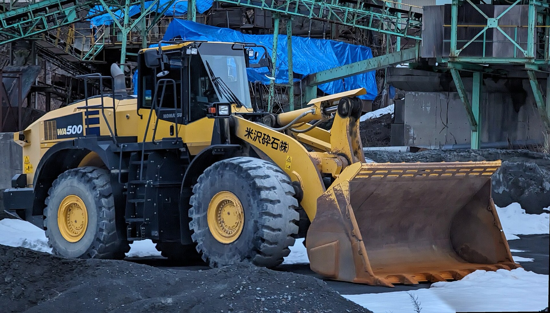 A yellow wheel loader with an empty bucket in a gravel yard